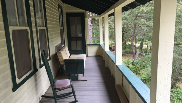 A porch with a rocking chair and a bench, wooden floor, and a view of trees. - Historic Oak Bluffs home, short walk to town, beach, and harbor. (Oak Bluffs)