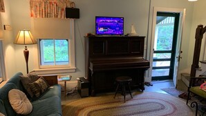 A living room with a blue sofa, a wooden coffee table, a television on a stand, a piano, and a patterned rug. - Historic Oak Bluffs home, short walk to town, beach, and harbor. (Oak Bluffs)