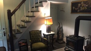 A staircase with glass railings, a green upholstered chair, a table with a lamp, a vintage stove, and a painting on the wall. - Historic Oak Bluffs home, short walk to town, beach, and harbor. (Oak Bluffs)