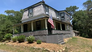 A two-story house with a porch, an American flag, and a stone retaining wall. - Historic Oak Bluffs home, short walk to town, beach, and harbor. (Oak Bluffs)