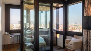 Una camera moderna con un divisorio in vetro, una sedia bianca, una scrivania e vista sulla città.