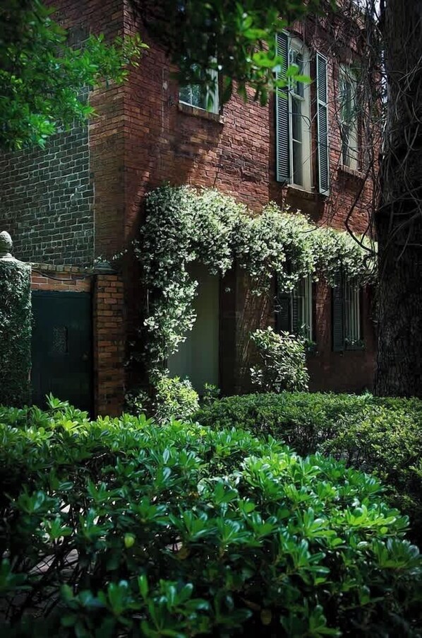 A brick building with green shutters, ivy-covered walls, and a statue in the foreground.