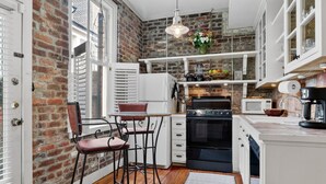 Una cocina con pared de ladrillo, armarios blancos, estufa y cafetera.