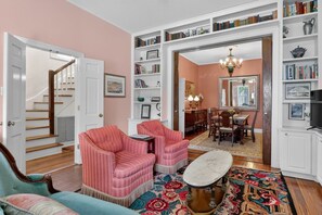 A living room with a staircase, a dining area, and a bookshelf filled with books.