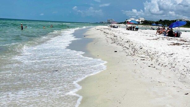 Une plage avec un ciel dégagé, une eau calme et peu de monde.