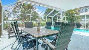 Une terrasse extérieure couverte, équipée d’une table de billard, de chaises et offrant une vue sur une piscine et sur la verdure.