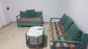 Une petite pièce avec un canapé vert, un fauteuil assorti et une petite table sur laquelle repose un coussin.