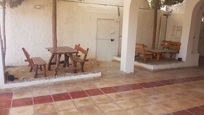 Un espace extérieur aménagé avec une table et des chaises en bois, un banc et un sol carrelé.