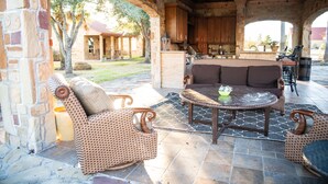 An outdoor patio area with wicker furniture, a stone fireplace, and a view of the backyard. - Cowboy corral 2 (Brenham)