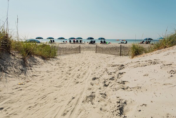 Une plage de sable avec une clôture en bois, des parasols et un ciel dégagé.