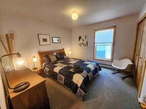 A bedroom with a bed, a desk, a chair, a window, and artwork on the walls.