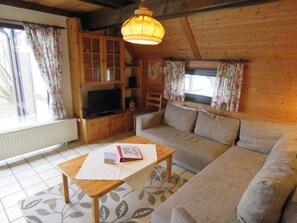 Un salon chaleureux avec un canapé en bois, une télévision et une table sur laquelle se trouvent un livre et des papiers.