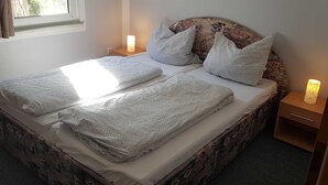 A bed with a patterned headboard, two bedside tables with lamps, and a window with curtains. - House 2 - Holiday home family Acker (Lychen)