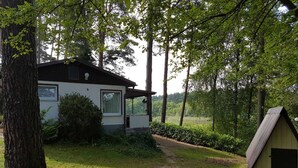 A house with a white exterior, a covered porch, and a small shed in a wooded area. - House 2 - Holiday home family Acker (Lychen)