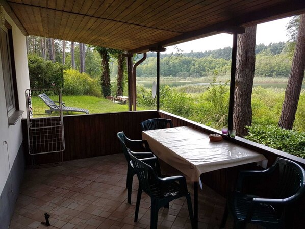 A covered patio with a table and chairs, overlooking a lush landscape with trees and a body of water. - House 2 - Holiday home family Acker (Lychen)