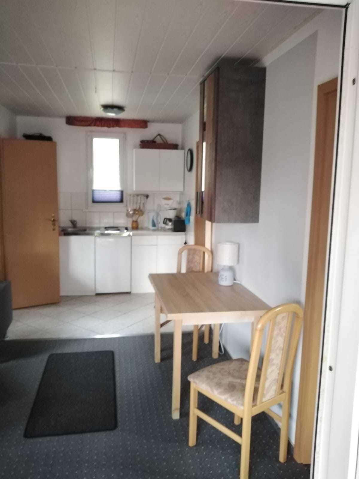 A compact kitchen with white cabinets, a wooden table, and a chair.