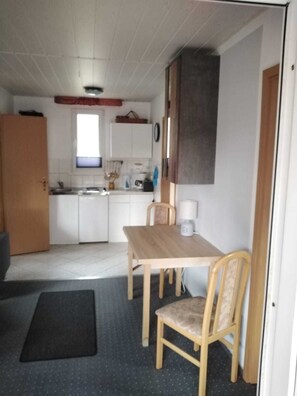A compact kitchen with white cabinets, a wooden table, and a chair.