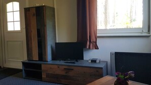 A room with a wooden cabinet, a television, a small table with a vase, and a window with curtains. - House 2 - Holiday home family Acker (Lychen)