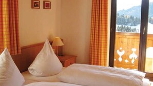 Habitación de hotel con cama, almohadas, mesita de noche, lámpara y ventana con vistas a las montañas.