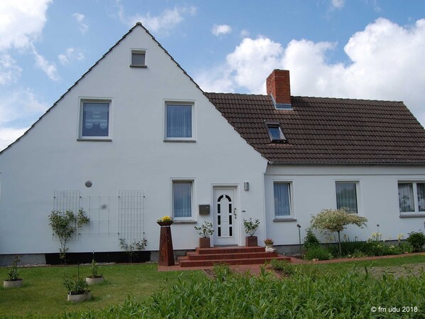 A two-story house with a triangular roof, a brick chimney, and a front door with steps leading up to it.