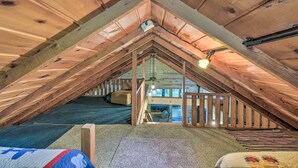 Un dormitorio en el ático con techo inclinado, vigas de madera, una litera, un escritorio pequeño y una ventana con vistas al exterior.