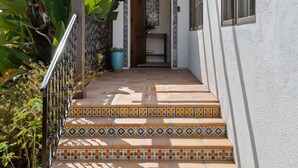 Una scalinata con piastrelle decorate conduce a una porta, circondata da piante e una pergola.