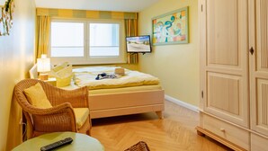 A hotel room with a bed, a chair, a table, a wardrobe, and a television. - Apartment 01 - House By the sea (Heringsdorf)