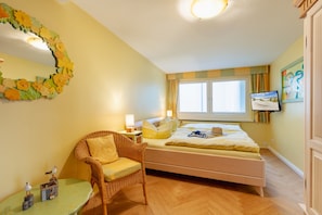 A bedroom with a bed, a chair, a table, a mirror, and a window.