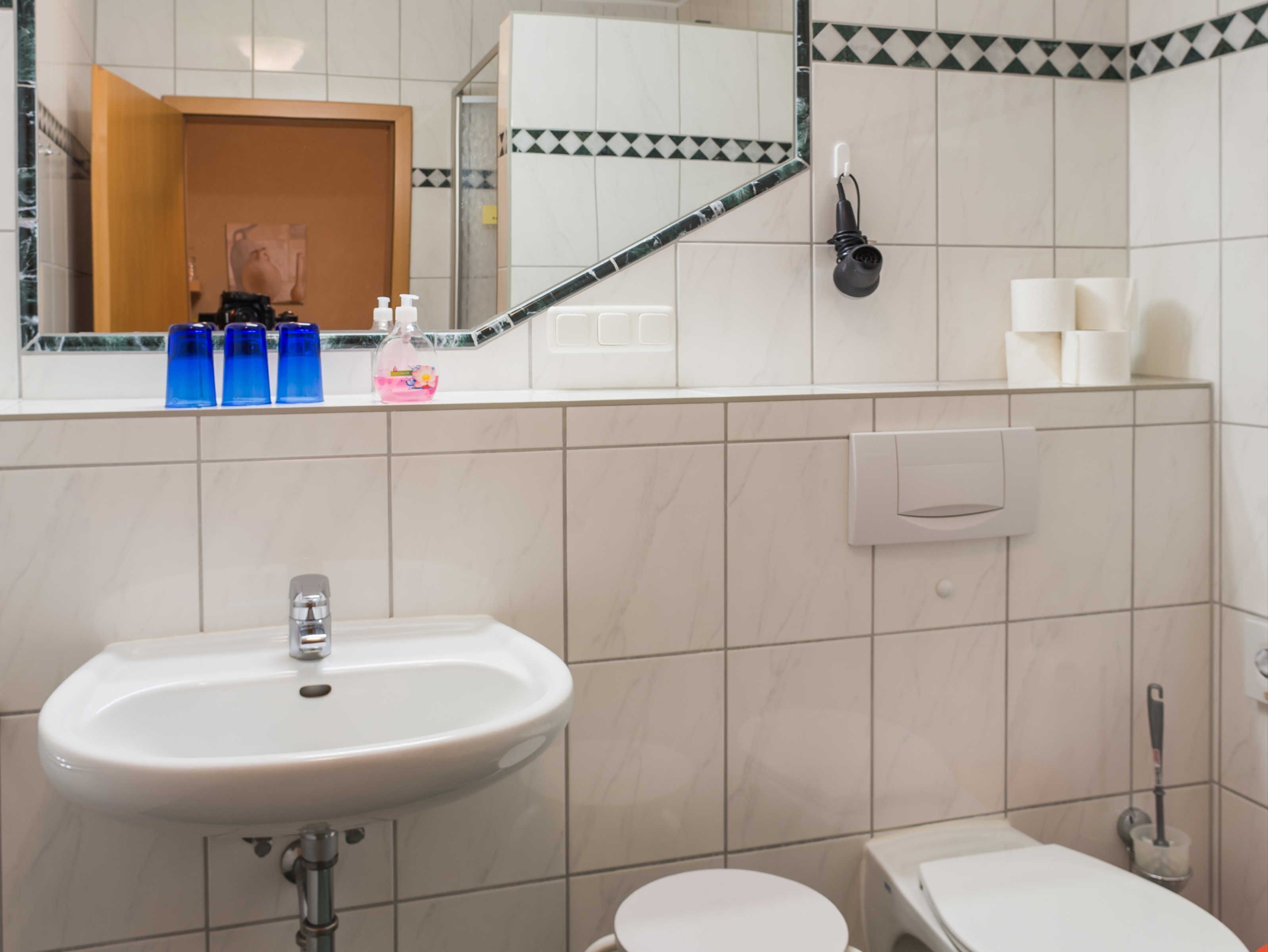 A bathroom with a sink, toilet, and a mirror reflecting a door and toiletries.