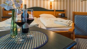 A hotel room with a bed, a nightstand, a lamp, a chair, and a table with wine glasses and a bottle. - Family room PG0802 - Pension Maiglöckchen (Karlshagen)