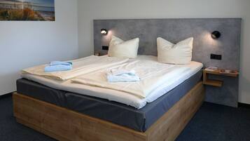 Ein ordentlich bezogenes Bett mit Kissen und Handtüchern, ein Nachttisch mit einem Buch und eine Wandleuchte.