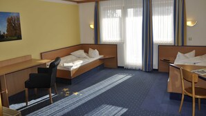 A hotel room with a bed, desk, and chair. There is a window with curtains, a painting on the wall, and a carpet with a star pattern. - Double room TWIN (3) - sleep & go Hotel Magdeburg GmbH (Magdeburg)
