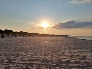 A beach with a sunset, a pier, and beach huts.