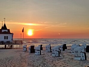 A beachside building with a flag, a pier, and beach chairs labeled with prices. - Double room 24 - Domkes Hotel Garni Haus an der See (Heringsdorf)