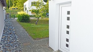 A narrow pathway leading to a white building with a garage door, surrounded by a gravel path and a small tree.