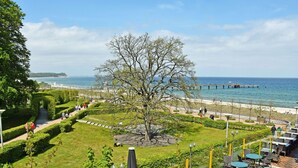A landscaped garden with a central tree, outdoor seating area, and a view of the sea.