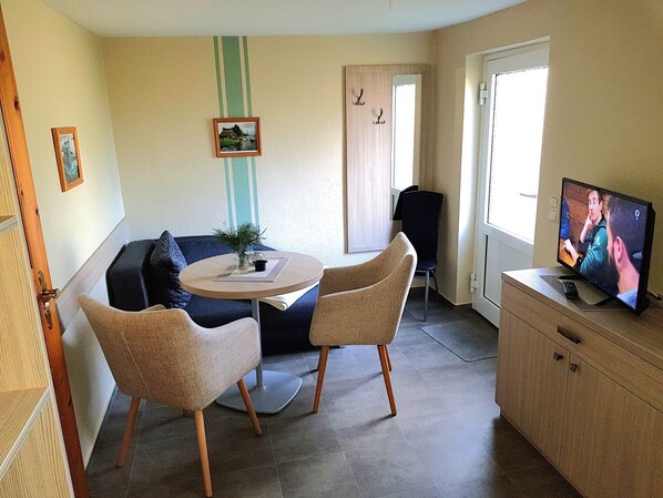 Un salon confortable avec une table ronde, deux chaises, un canapé, un téléviseur et une porte.