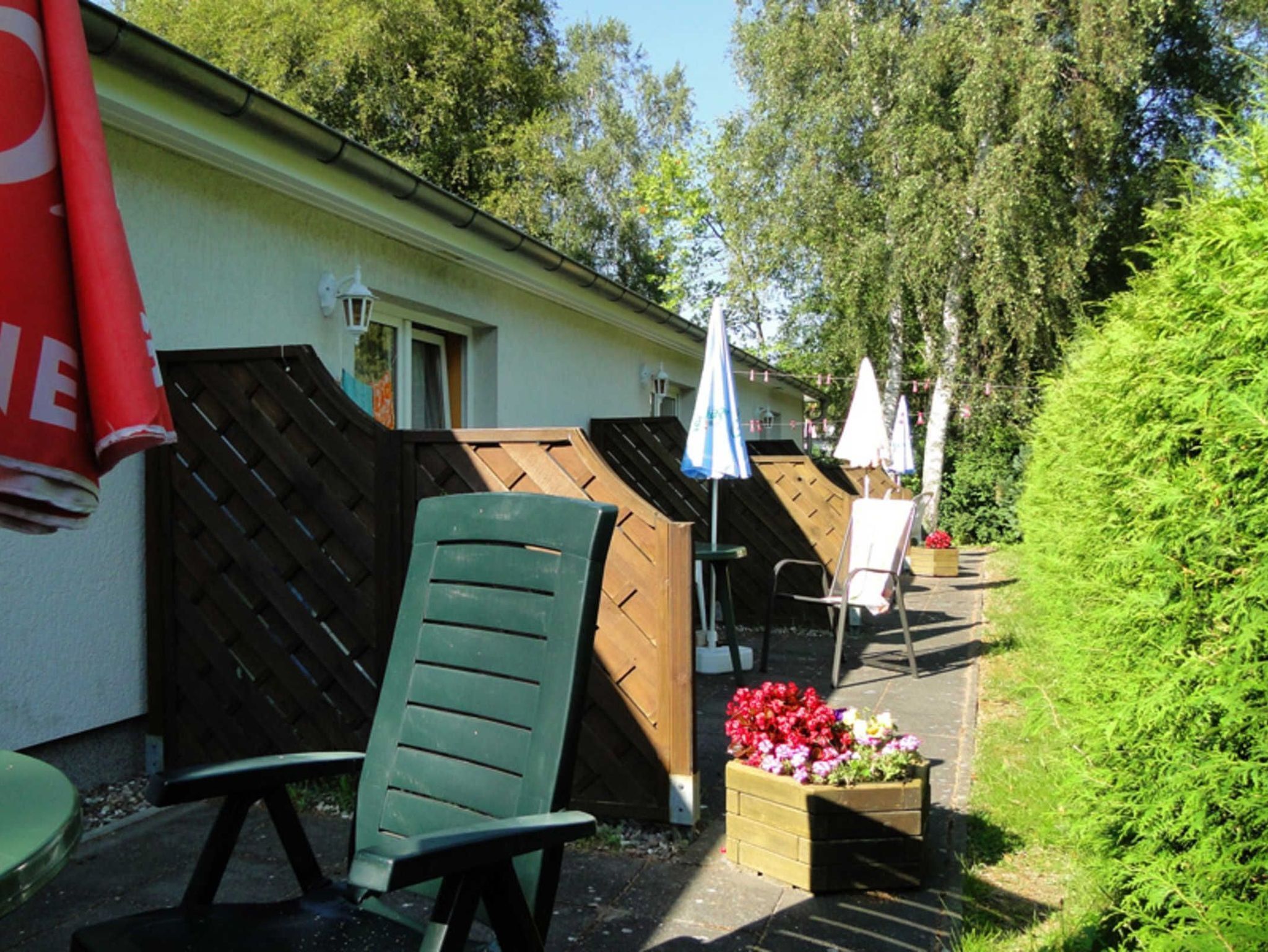 Eine Terrasse mit einem grünen Stuhl, einem hölzernen Pflanzkasten mit Blumen und einem weißen Sonnenschirm.