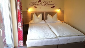 Un lit double avec une literie blanche, une tête de lit agrémentée d’un panneau décoratif mural et une fenêtre avec des rideaux rouges.