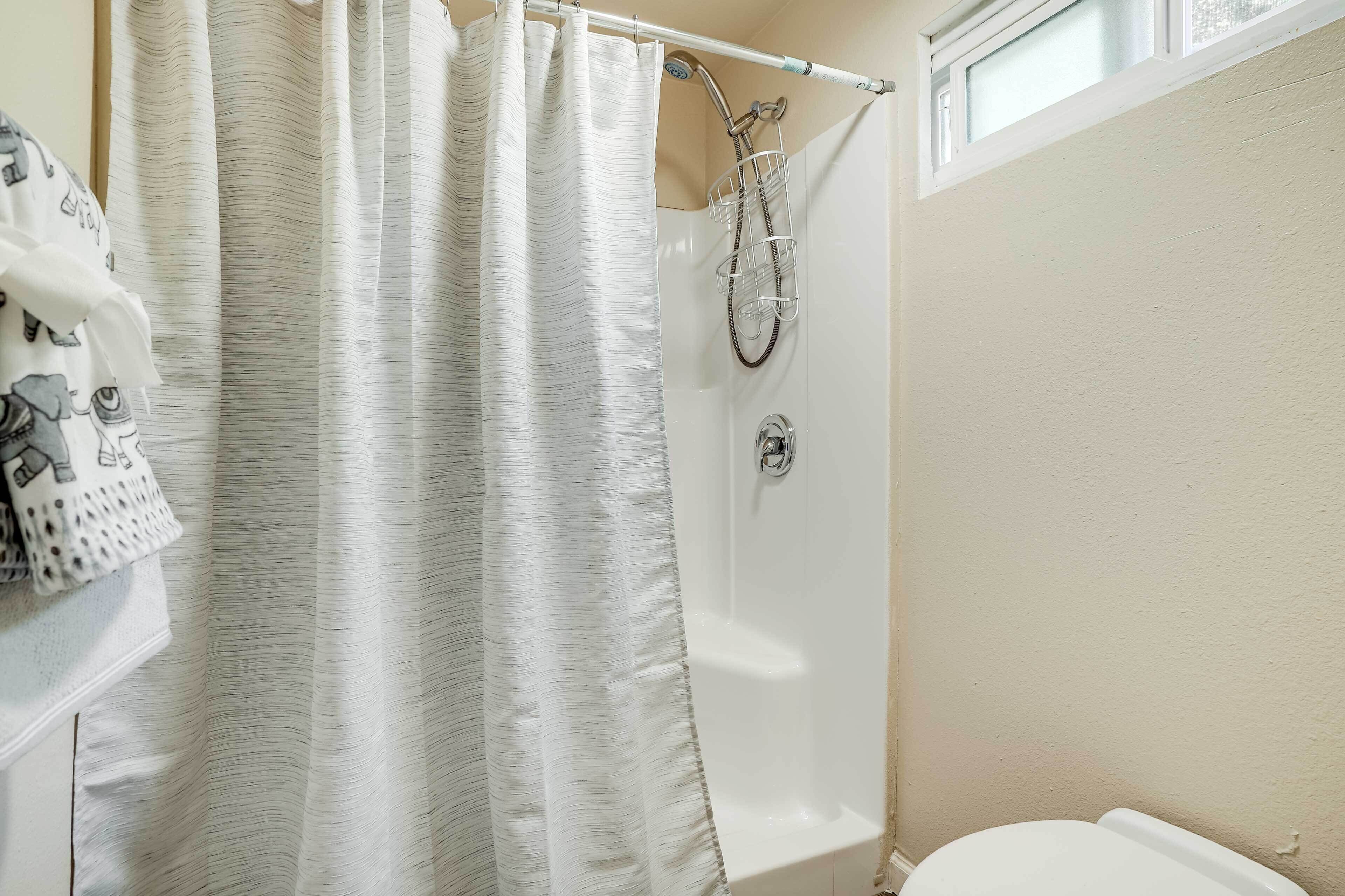 A bathroom with a shower, a towel rack with patterned towels, and a window above the shower.