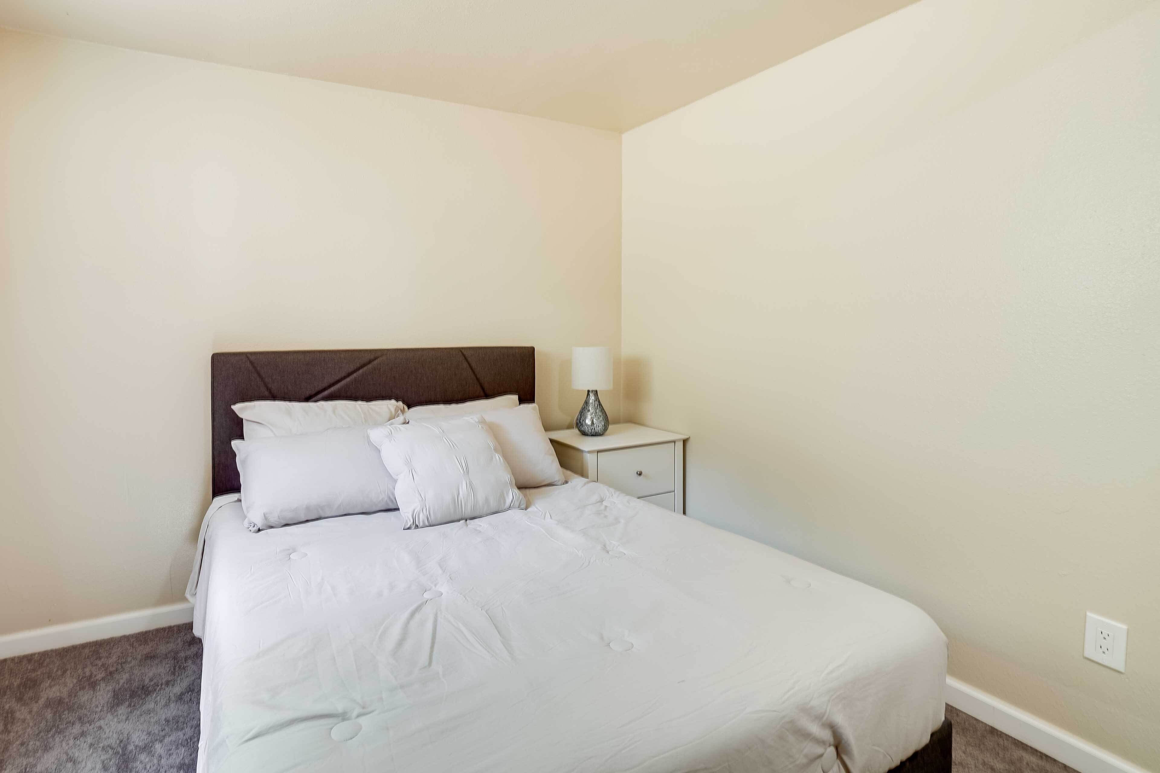 A neatly made bed with white linens and pillows, a bedside lamp, and a small bedside table.