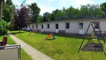 A grassy area with playground equipment, a picnic table, and a building with windows.