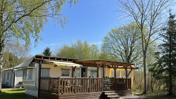 Ein Wohnmobil mit einer Holzterrasse und einer überdachten Veranda, umgeben von Bäumen.