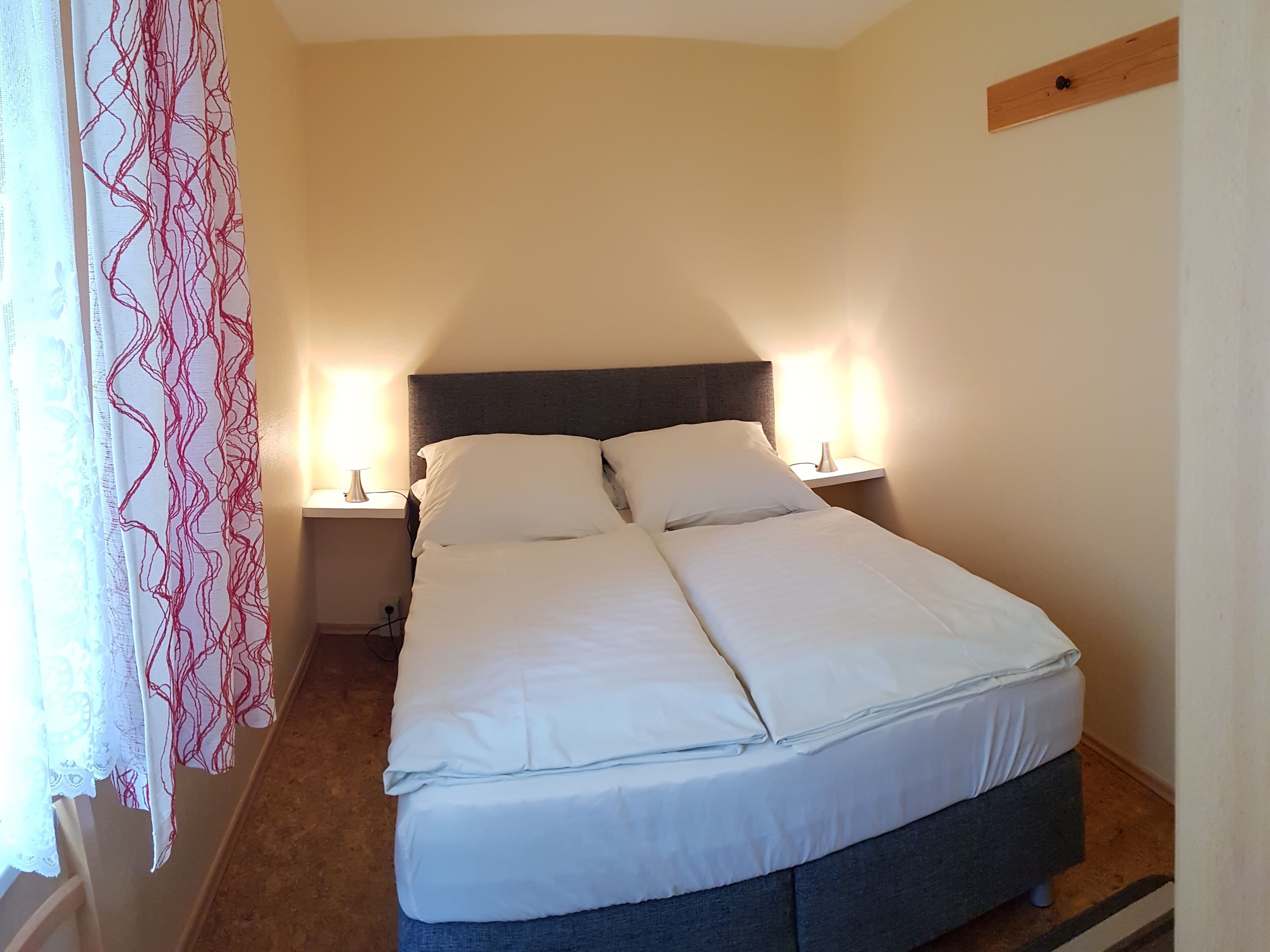 A double bed with white linens, two bedside lamps, and a wooden headboard.