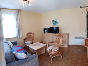 A living room with a sofa, two wicker chairs, a coffee table, a TV, and a cabinet.