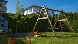 A backyard with a wooden swing set, a picnic table, and a house in the background. - Double room PK2005 - Pension Maiglöckchen (Karlshagen)