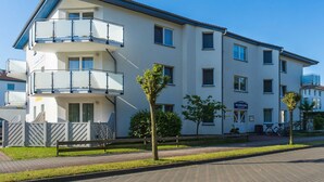 Un immeuble résidentiel à plusieurs étages, doté de balcons, d’une allée pavée et d’un petit arbre au premier plan.