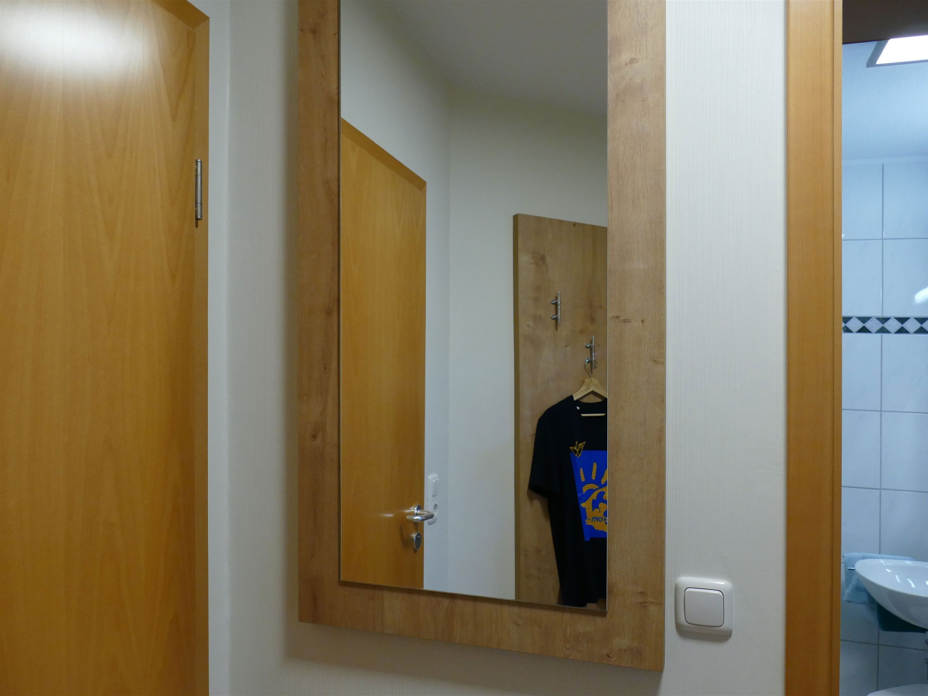 Eine Holztür mit Spiegel, eine weiße Wand und ein Badezimmer mit Waschbecken und gefliestem Rückspritzschutz.