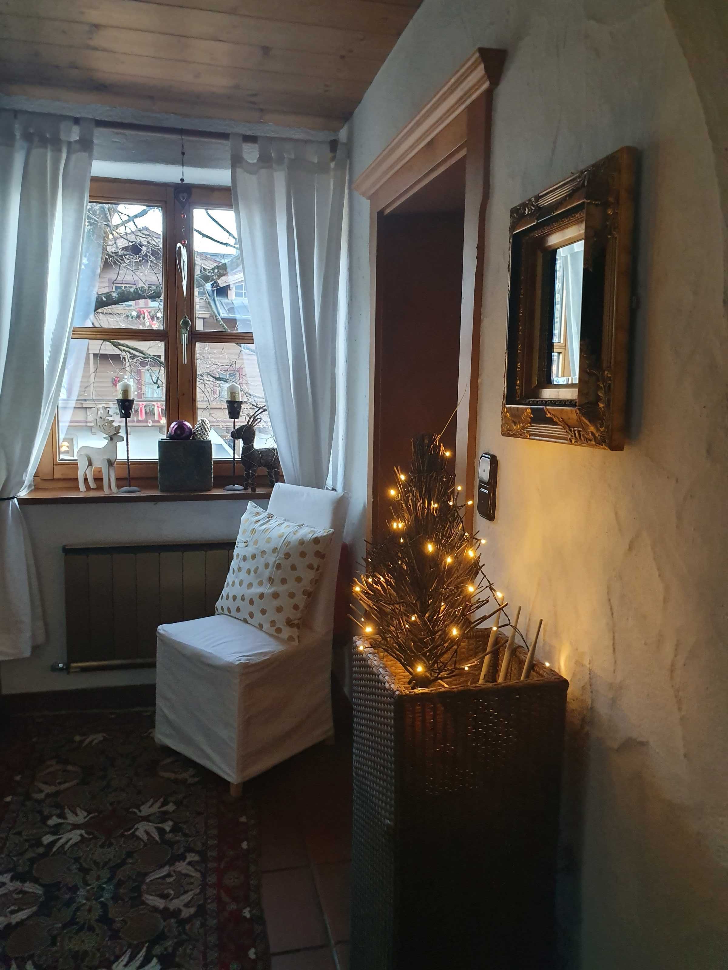 Een knus ogende kamer met een witte stoel, een radiator, een raam met gordijnen en een decoratieve spiegel aan de muur.