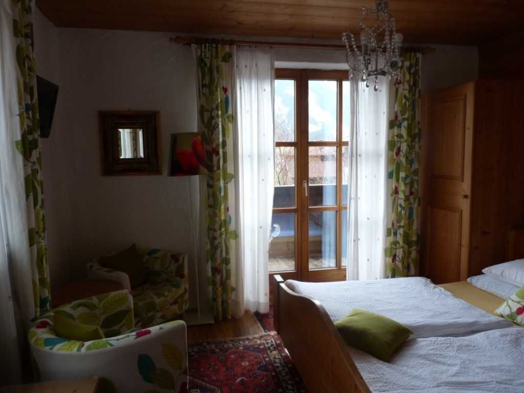 Un dormitorio con cama, una silla, un ventanal y una puerta.